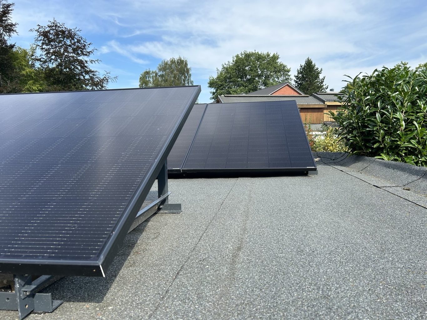 Nutzt die Sonne effizient! Ein Balkonkraftwerk ist einfach aufgebaut und senkt sofort die Stromrechnung. Solaranlagen auf einem Dach, umgeben von Bäumen und einem klaren Himmel.